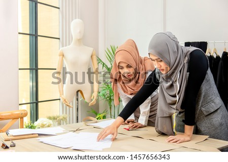 Young Asian muslim woman fasion designer working with colleague  in tailor shop Royalty-Free Stock Photo #1457656343