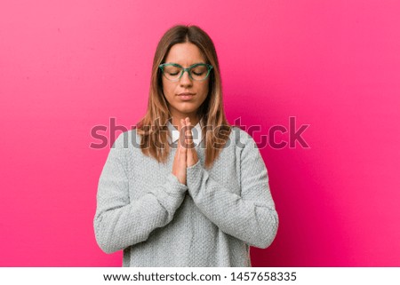 Young authentic charismatic real people woman against a wall holding hands in pray near mouth, feels confident.
