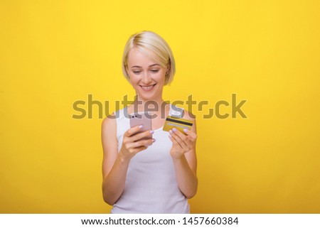 Shopping time, young blonde woman, using mobile and credit card, for online shopping, over yellow background 