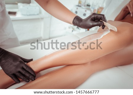 Special wax material. Attentive experienced cosmetologist working with wooden spatula while adding wax on the skin Royalty-Free Stock Photo #1457666777