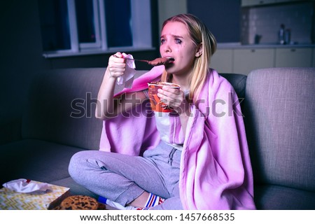 Young woman watching movie at night. Sad picture of model sitting on sofa and crying. Eating ice cream. Watching sad tv series and movie. Alone in room.
