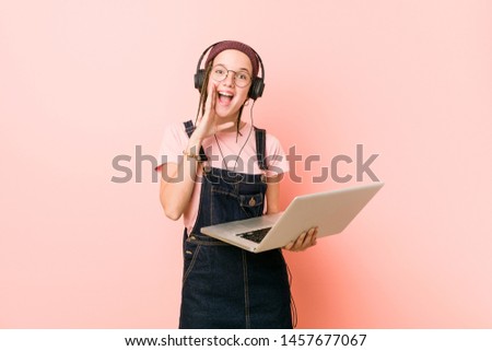 Young caucasian woman holding a laptop shouting excited to front.