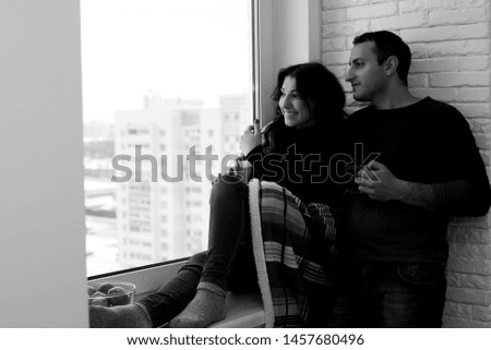 A young married couple looks out the window of a new apartment
