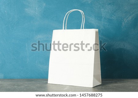 White paper bag on grey table against blue background, copy space