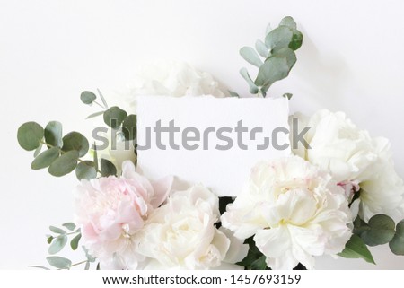 Feminine wedding, birthday mockup scene. Closeup of blank cotton paper card, invitation and floral bouquet. White and pink peonies flowers and eucalyptus. Styled stock photo. 