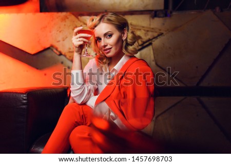 Photo of young blonde in red jacket and trousers with cocktail in her hand in nightclub