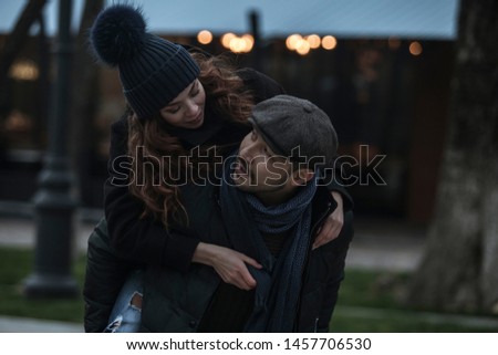 Young couple having fun outdoors at winter fair. Wearing warm clothes, hats and scarfs. Visiting christmas market in Vienna, Austria. Everything is decorated with festive string lights.