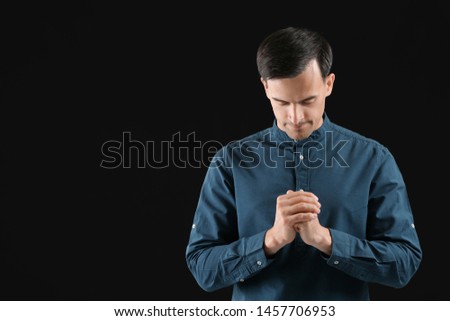 Religious man praying to God on dark background