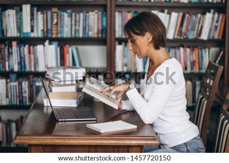 Young woman sitting at the library using books and computer