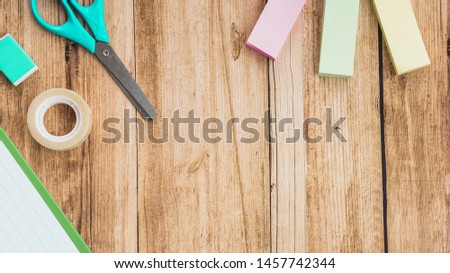 Sticky notes; scissor; tape and eraser on wooden table