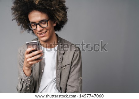 Photo of handsome caucasian man with afro hairstyle smiling and looking at cellphone isolated over gray background