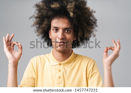 Photo of relaxed caucasian man with afro hairstyle meditating and keeping fingers in zen gesture isolated over gray background