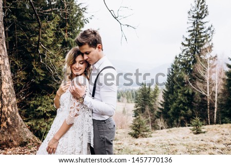 Portrait of the happy young Caucasian couple of just-married man and woman in the wedding clothes hugging and posing to the camera in the mountaince on the fall day.