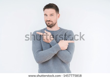 Young handsome man wearing casual sweater over isolated background Pointing to both sides with fingers, different direction disagree