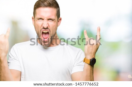Handsome man wearing casual white t-shirt shouting with crazy expression doing rock symbol with hands up. Music star. Heavy concept.