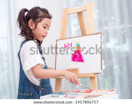 Little asian cute girl 6 years old playing watercolors painting cake for happy birthday on white paper. Learning and education of kid.