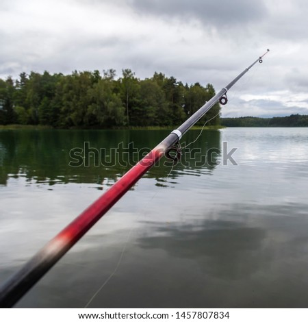 Closeup of fishing rod during fishing time near river. Beautiful water picture about fishing with clouds.  Square photo