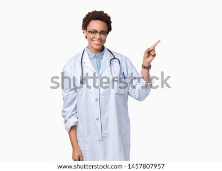 Young african american doctor woman wearing medical coat over isolated background with a big smile on face, pointing with hand and finger to the side looking at the camera.
