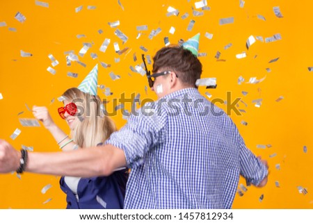 Fun, holidays and party concept - Couple dancing among falling confetti on yellow background