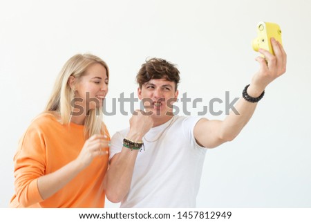 Funny crazy young couple blonde girl and a hipster guy taking a selfie on a vintage yellow film camera posing on a white background. Concept of photography hobby.