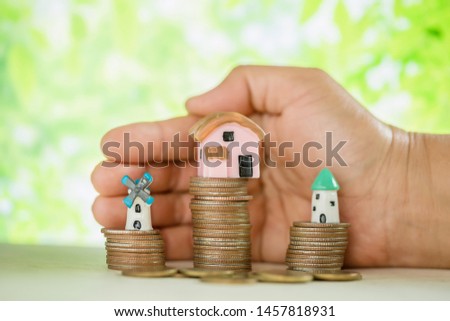 Hand pampered coins and small house model on green blur background.