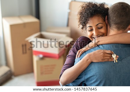 Young african woman holding home keys while hugging boyfriend in their new apartment after buying real estate. Lovely girl holding keys from new home and embracing man. Couple around cardboard boxes. Royalty-Free Stock Photo #1457837645