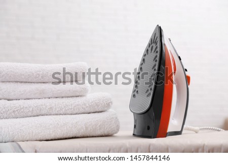 New modern iron and clean towels on board against light background. Laundry day