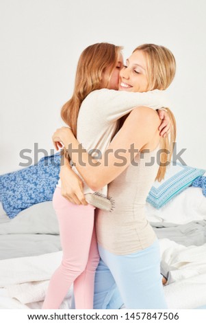 Girl hugs and kisses her mother lovingly on the bed in the bedroom
