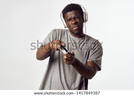 Cute African American in headphones with a game joystick from the console and in a gray T-shirt