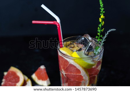 refreshing glass of water with fresh slice of grapefruit, lemon and ice on a dark background