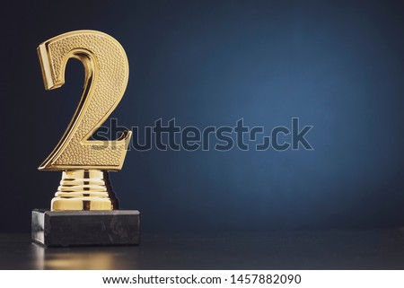 Second place winners gold trophy with a 3D textured metallic number two over blue with copy space