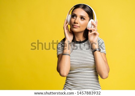 Gorgeous brunette lady listening music in headphones and singing on yellow background