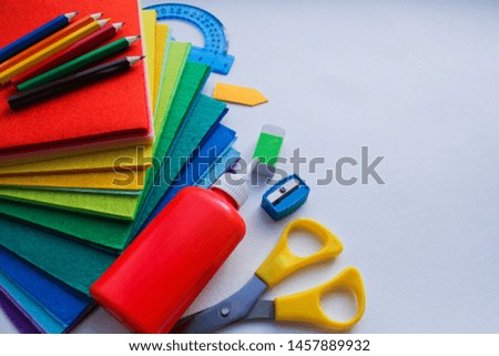Flat lay of stationery for school and creativity, drawing and crafts (watercolor paints, colored pencils, colorful pieces of felt) is on the left against a white watercolor paper with space for text