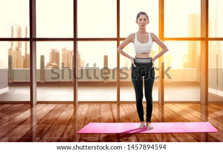 Asian healthy woman practicing yoga on the carpet at indoor with windows glass and city background