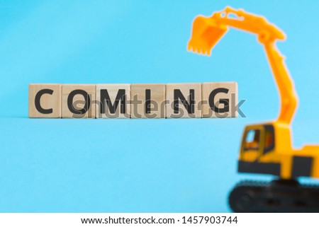 coming wooden cubes letters yellow toy excavator, development page under construction or technical work concept blue background