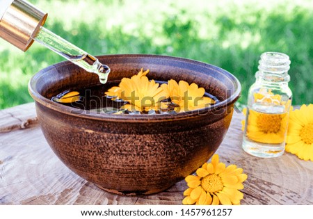 Aromatherapy essential oil with calendula flowers on a wooden background in nature. Extract of calendula tincture in a bowl. Medicinal plants.