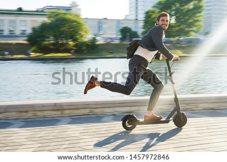 Young business man in a suit riding an electric scooter on a business meeting. Ecological transportation concept Royalty-Free Stock Photo #1457972846