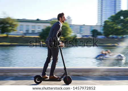 Young business man in a suit riding an electric scooter on a business meeting. Ecological transportation concept Royalty-Free Stock Photo #1457972852