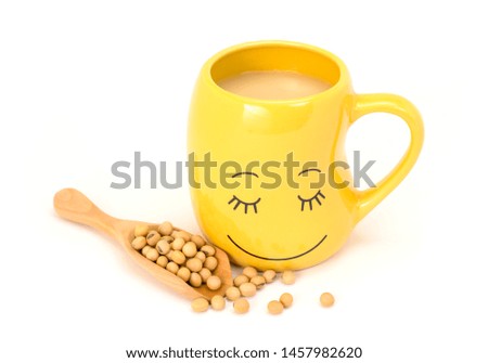 Emotional cup in bean shaped with smile face. Close up smiling cup of soy milk with soy beans in wooden spoon isolated on white background. Healthy food and drinks for wellbeing concept. 