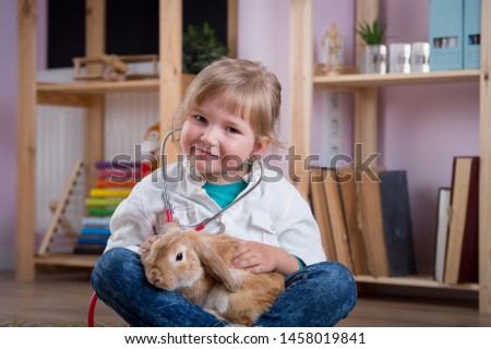 Child playing veterinarian doctor with rabbit. Happy smiling kid girl at home or daycare. Pediatrician. Preschool, school and kindergarten kids take care about animal. Pediatric, healthcare 