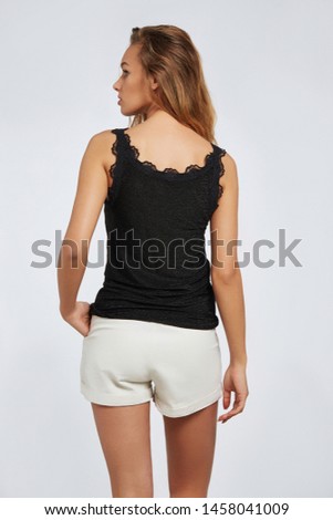 Cropped bottom back view shot of a young lady with blonde wavy hair. The fashion model with a natural make-up is dressed in white shorts and black tank top with fretted lace. 
