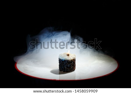 Candle with flame and jets of smoke on a black background. Original candle with fire in the blue smoke. Beautiful background. Coffee. Coffee grains on a candle. Beautiful wallpaper. Contemporary art. 