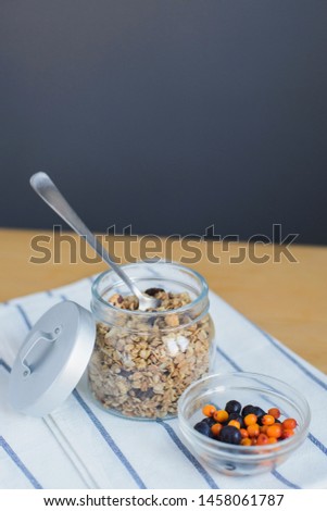 sea buckthorn and blueberry berries, granola with nuts and oat flakes near in glass bowl on striped textile napkin on wooden table, close up view from above of vertical still life stock photo image