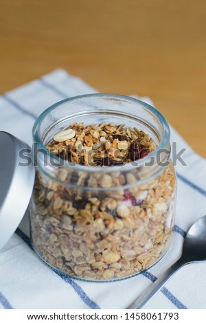 granola with peanuts, hazelnuts, oat and wheat flakes in glass bowl on striped textile napkin on wooden table, close up view from angle above of vertical still life stock photo image