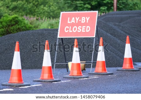 Road lay by closed sign with pile of black tar and red traffic cones