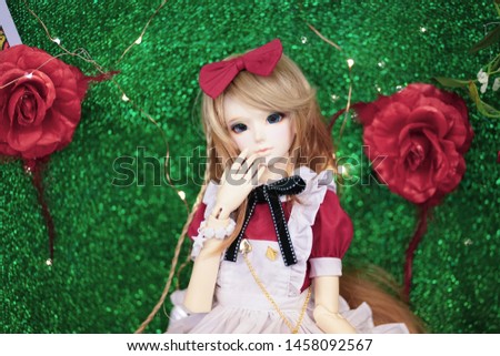 Cute BJD doll. BJD stands for Ball-Jointed-doll. A doll dress up in lovely red maid dress and braided hair. red roses on the background for wonderland concept.