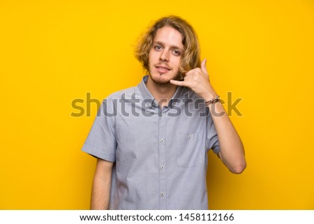 Blonde man over isolated yellow background making phone gesture. Call me back sign