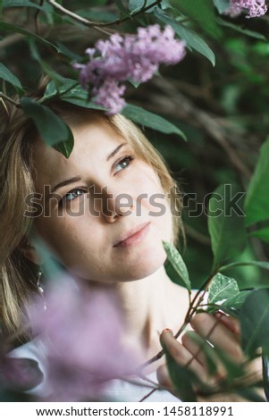 Portrait of a cute young woman surrounded by lilac flowers. Close-up