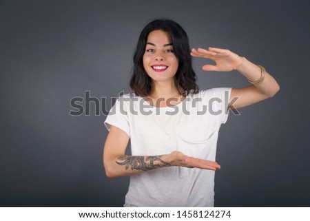 Brunette European woman over isolated background gesturing with hands showing big and large size sign, measure symbol. Smiling looking at the camera. Measuring concept.