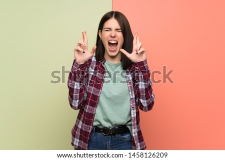 Young woman over isolated colorful wall with fingers crossing